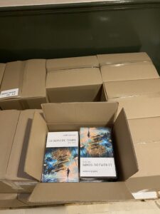 Une palette de cartons, dont un ouvert et l'on voit des livres épais sous blister, intitulés Le repli du Temps de la romancière Judith Lossmann